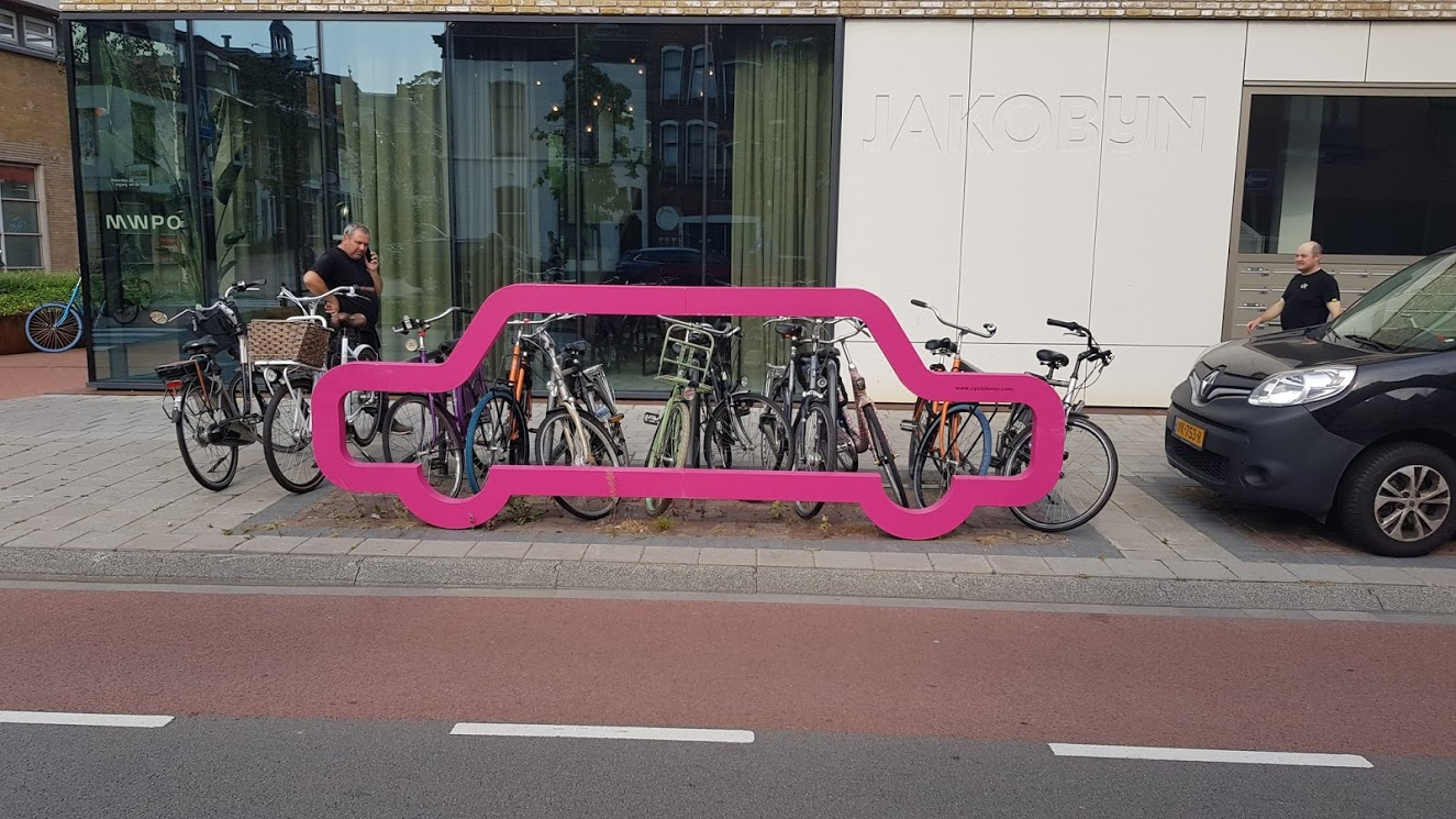 Picture of a bike rack in the shape of the outline of a car, with 9 bikes locked to it