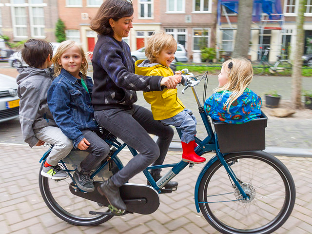 Woman biking with 4 children on a bicycle – 2 in front, 2 in back