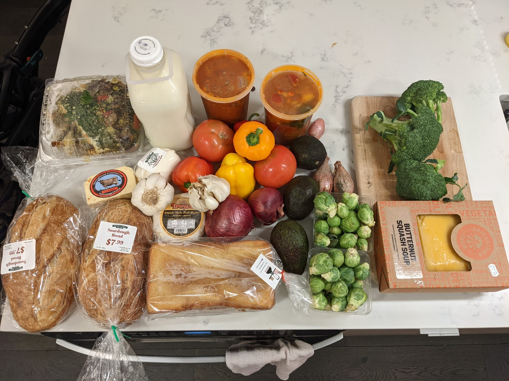 Groceries on counter-top: bread, soup, sauce, vegetables, cheeses