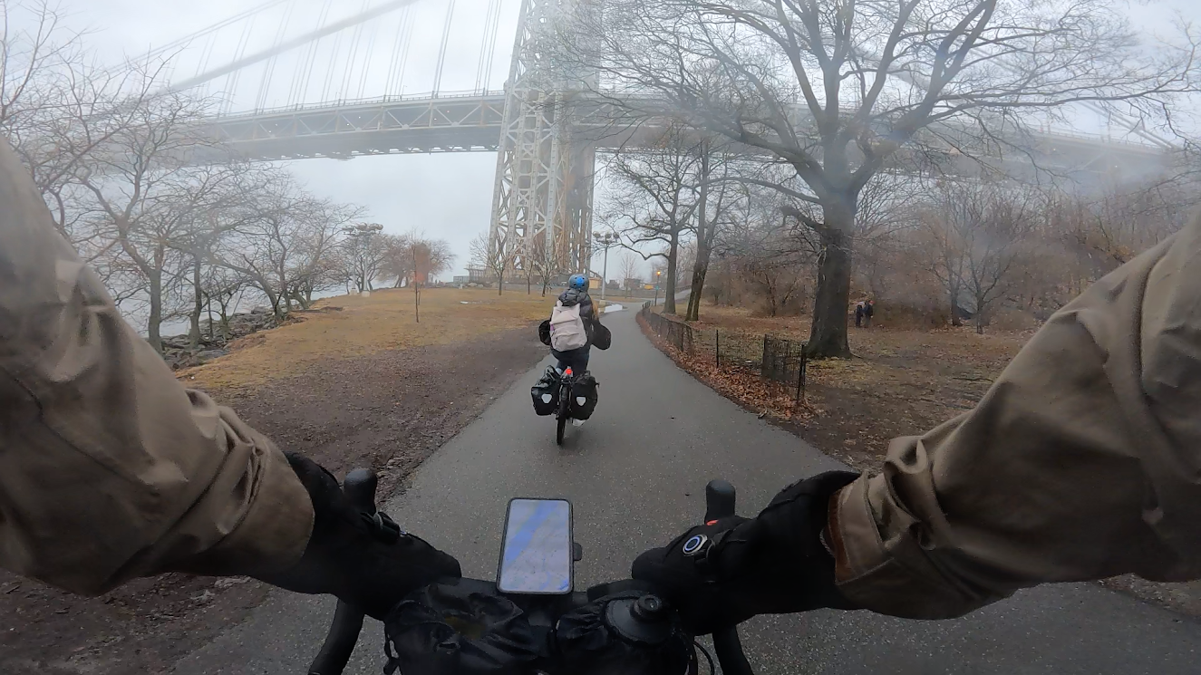 Chest-cam shot of phone mounted on handlebars displaying a Google Map, another e-biker is in front, and the George Washington Bridge is in the background