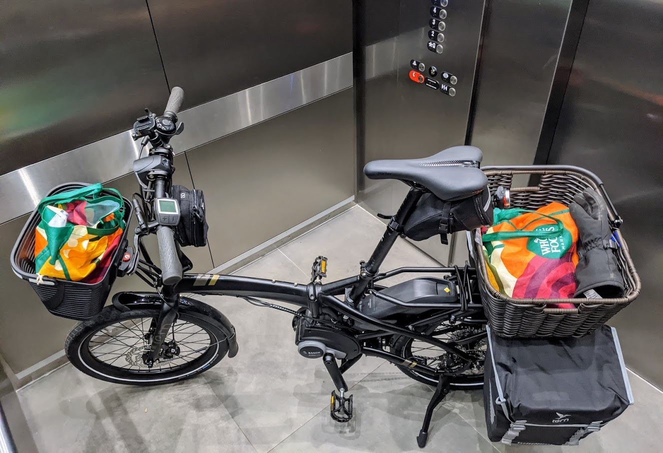 Tern Vektron Q9 in elevator with two full panniers and front and rear baskets with grocery bags